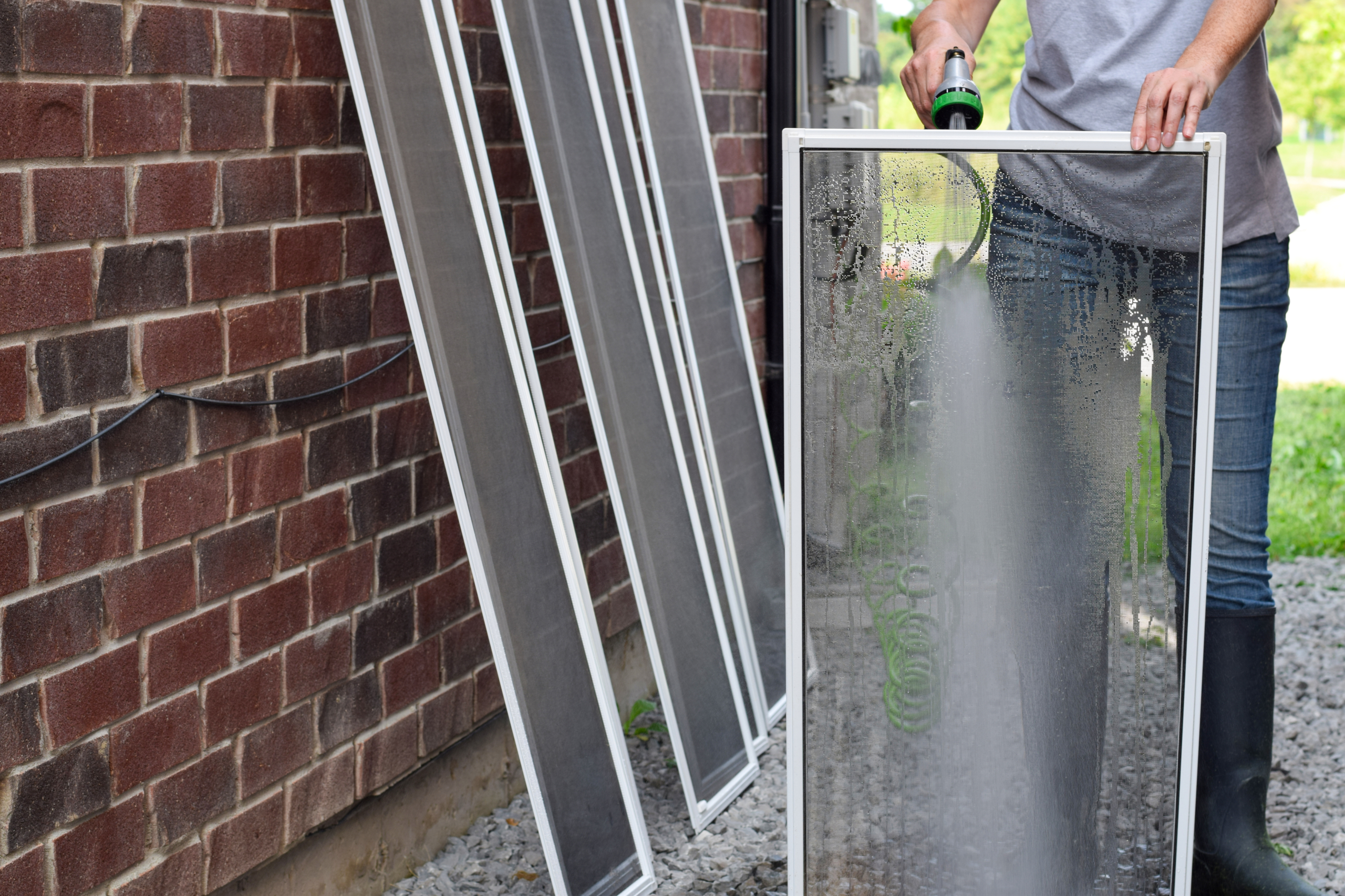 Woman cleaning window and patio door screens with water hose outside for Memorial Day weekend